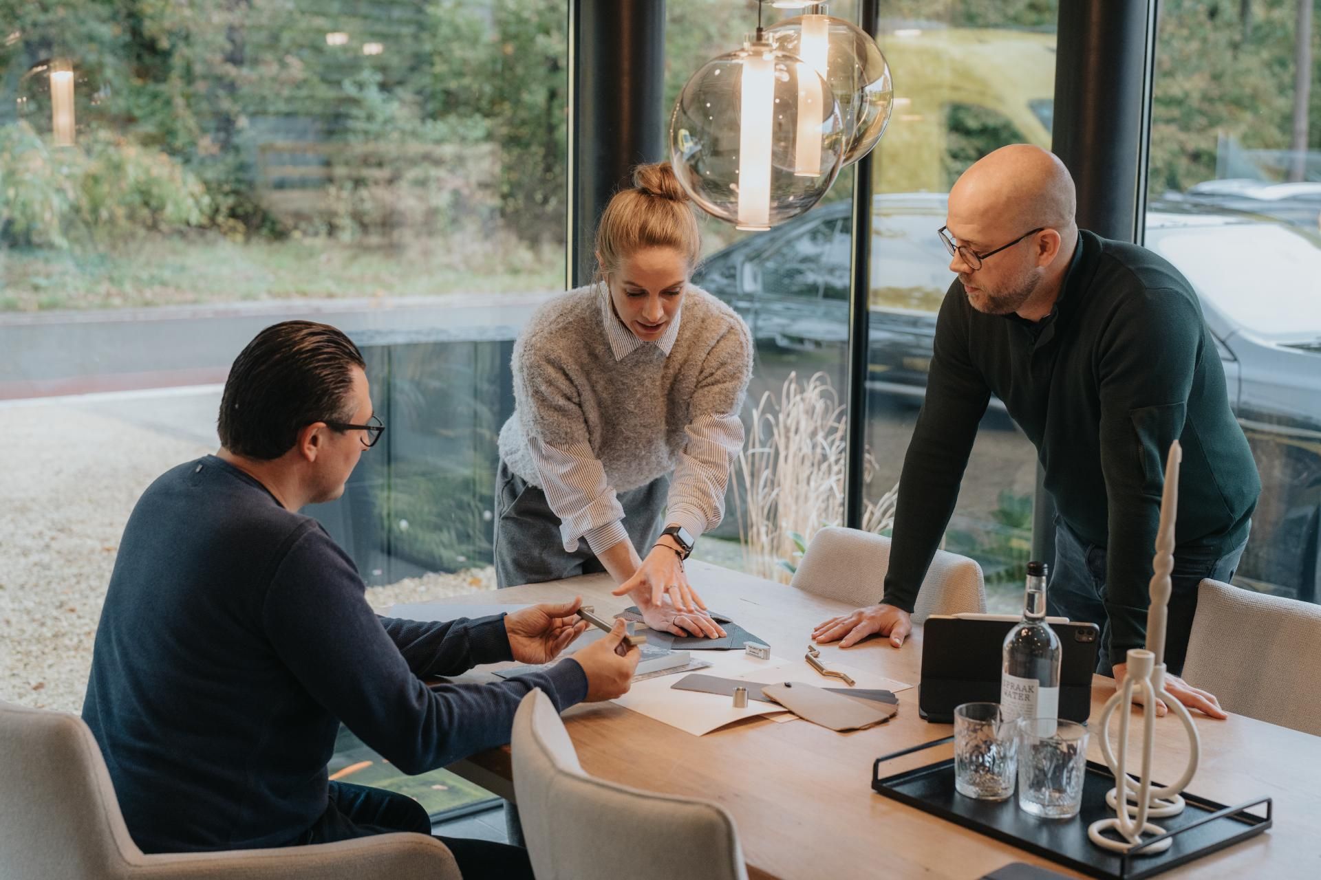 Een inspirerend gesprek aan een houten tafel met kleurstalen en materialen, waar een interieurontwerper klanten adviseert over een nieuw interieur op maat.