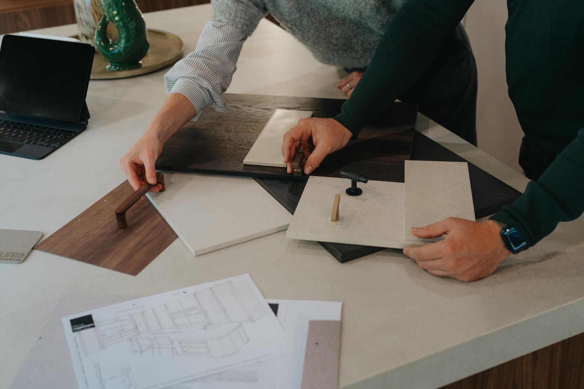 Twee personen selecteren materialen voor een maatwerk interieur. Op de tafel liggen verschillende houtstalen, handgrepen en steenoppervlakken, zorgvuldig gekozen voor een keuken of meubelontwerp.