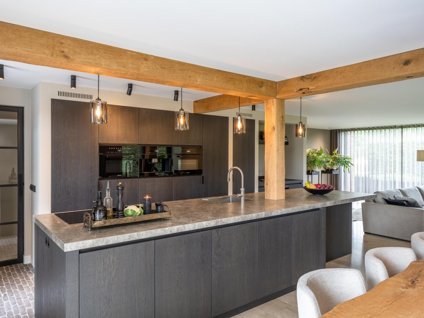 Een stijlvolle, moderne keuken met donkere maatwerk kasten, een robuust werkblad en houten balken. De combinatie van industriële en natuurlijke materialen zorgt voor een luxe uitstraling.