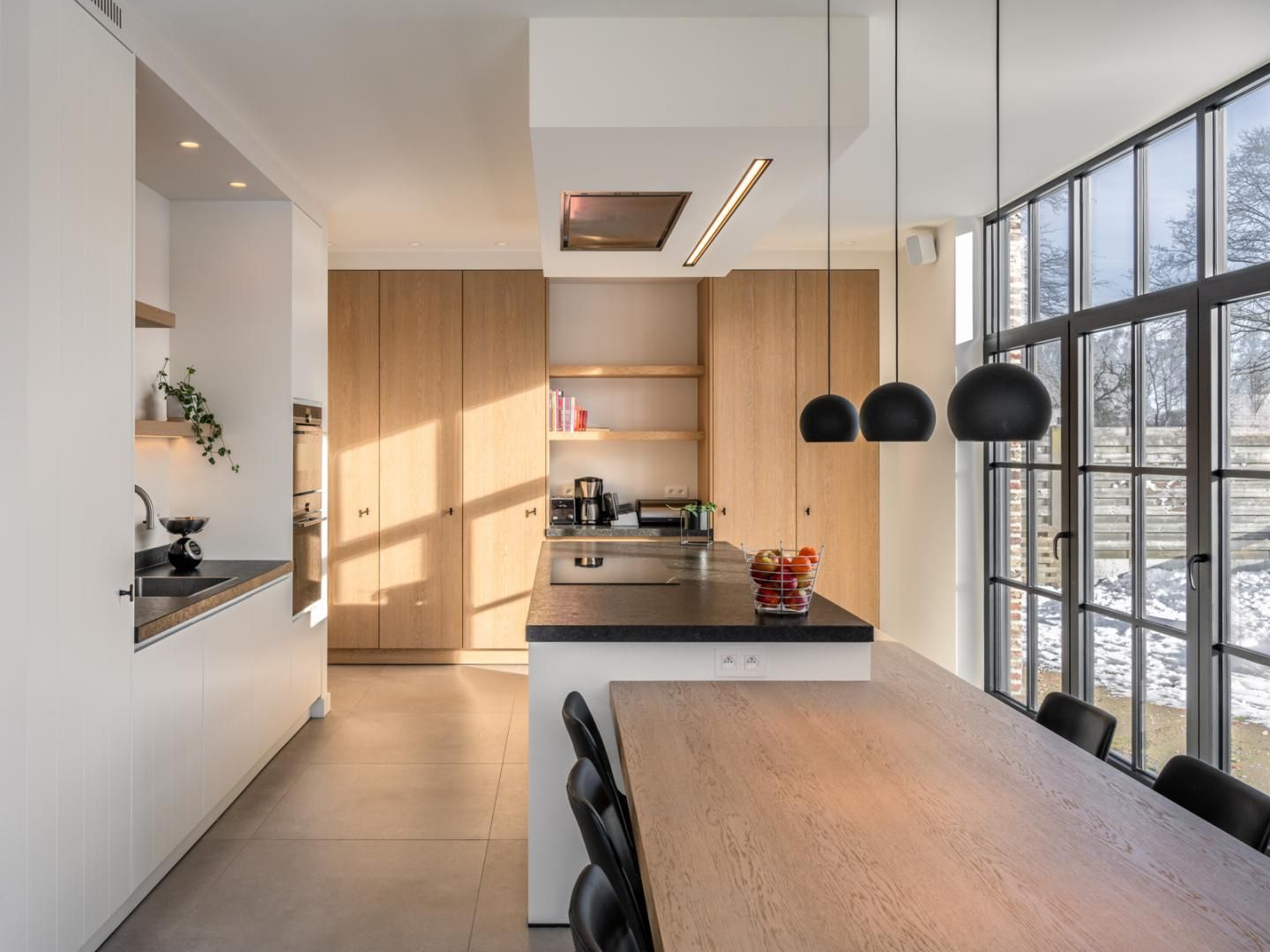 Een moderne keuken met veel natuurlijk licht, een groot keukeneiland en op maat gemaakte houten kasten. De open indeling en zwarte accenten geven een tijdloze uitstraling.