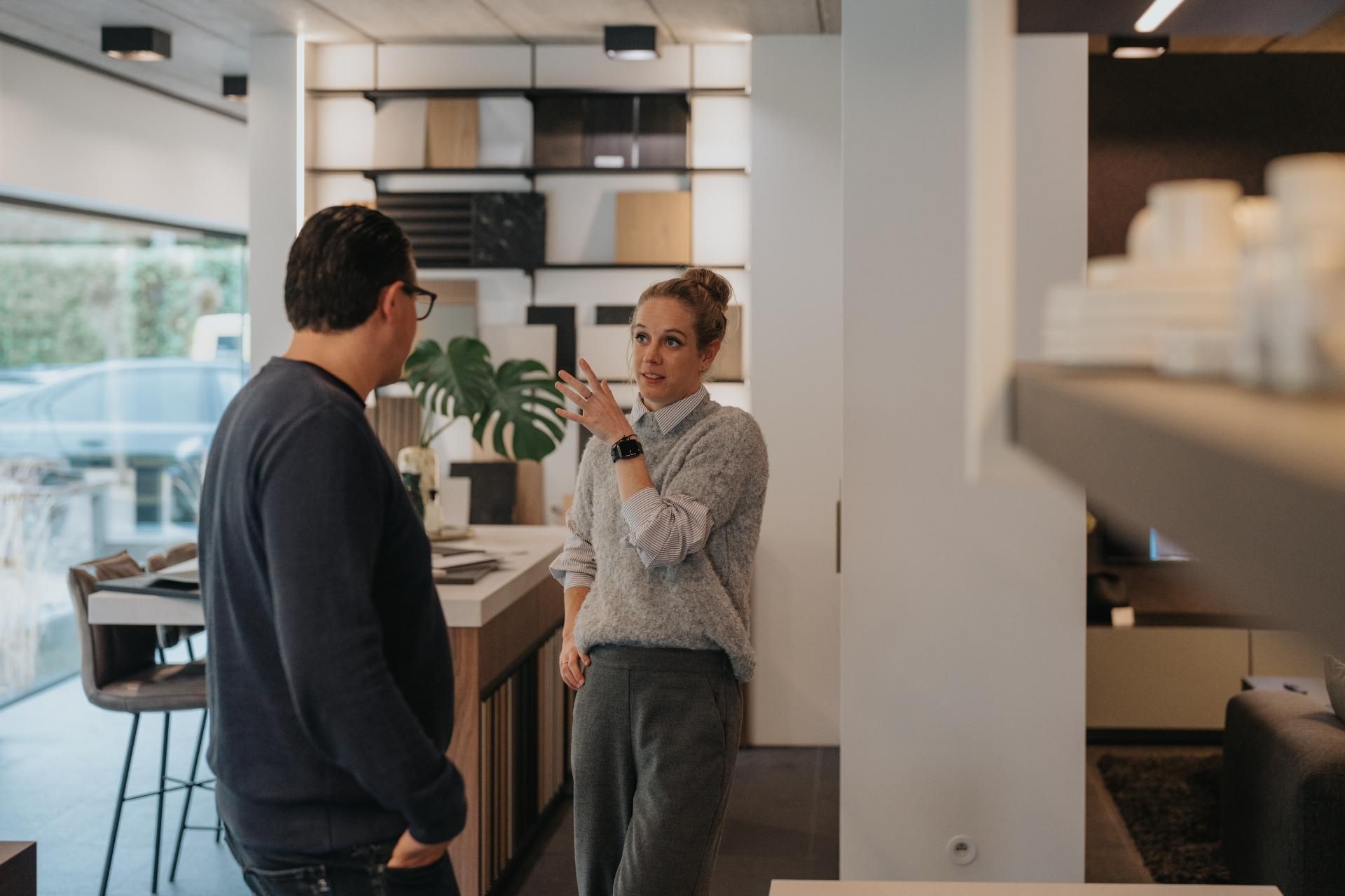 Een interieuradviseur bespreekt ontwerpmogelijkheden met een klant in een showroom vol houtstalen en maatwerkoplossingen. De open en moderne ruimte benadrukt de persoonlijke begeleiding en expertise in interieurdesign.